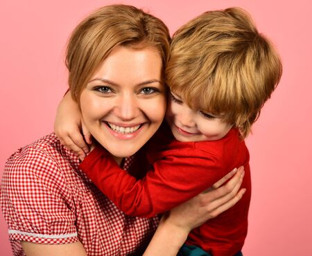 Mother hugs son on pink background. Family happiness concept