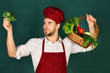 Chef in burgundy uniform looks at broccoli an hand.