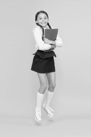 Emotional pupil. Excited about studying. Happy child jumping in school uniform. Having fun. Jumping and feeling free. Back to school concept. Little girl yellow background. School girl likes to studyの写真素材