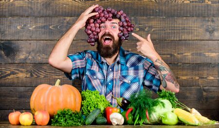 Farming concept. Man hold grapes wooden background. Farmer bearded guy with homegrown harvest grapes put on head. Farmer proud of grapes harvest. Fresh organic harvest. Grapes from own garden.の写真素材