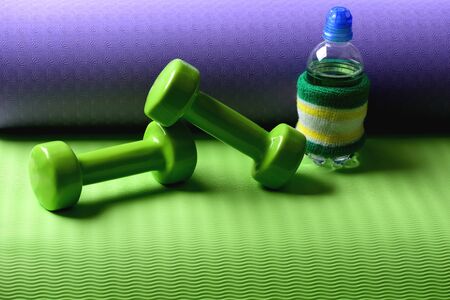Sports and healthy lifestyle concept. Water bottle with hand band and dumbbells made of green...