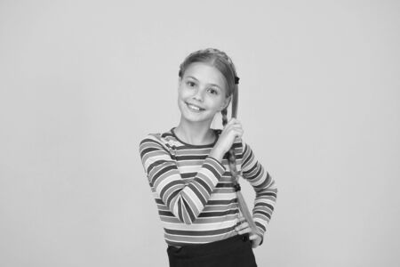 Braiding hair. Adorable little girl with plaited hair yellow background. Cute small child hold long hair braid. Luxurious hair extensions. Beauty salon. Haircare and hairstylingの写真素材