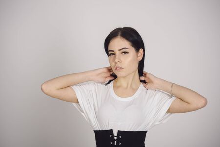 Woman on mysterious pensive face posing. Lady in stylish dress with wide black belt on waist. Young beautiful female model in white dress on gray background. Fashionable outfit concept.の写真素材