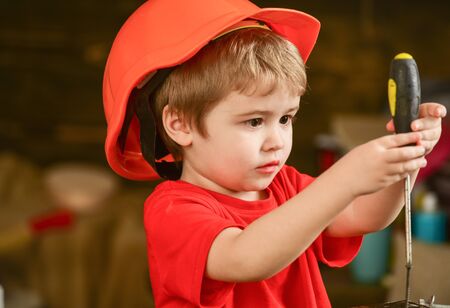 Closeup blond kid with screwdriver in workshop. Boy binding screws to wooden block. Concentrated...