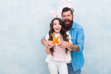 having fun in rabbit costume. dad and child wear bunny ears. carrot for my little rabbit. copy space. Spring mood. easter family party. happy easter concept. father and daughter eating healthy foodの写真素材
