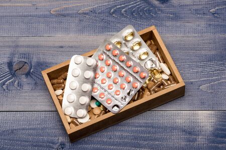Medicine set: antibiotics, cod liver, painkillers or vitamins for treatment. Prescriptions concept. Tablets or pills in blisters. Drugs of pink and transparent colors in box on grey wooden background.の写真素材