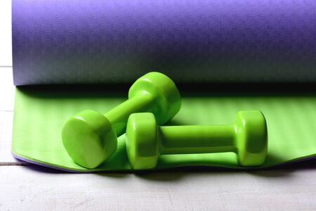 Dumbbells made of green plastic on green and purple texture background. Shaping and fitness equipment. Barbells lying on yoga mat, close up. Sports and healthy lifestyle conceptの写真素材