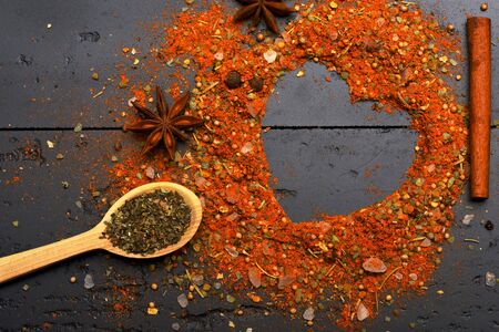 Wooden spoon with herbs, cinnamon stick and anise stars by scattered seasoning. Cuisine and flavour concept. Composition of condiment making heart shape. Set of spices on dark grey texture backgroundの写真素材