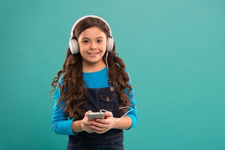 e-learning in modern life. schoolgirl use new technology. copy space. kid listen music in headphones. small child make play list on smartphone. small girl hold mp3 player. choosing favorite songの写真素材