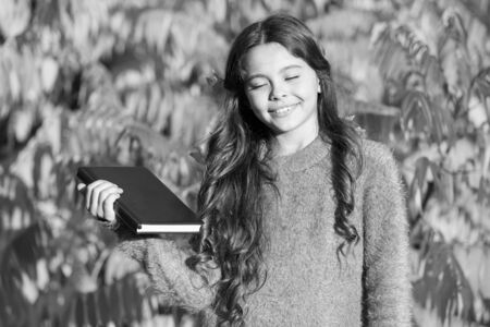 Autumn literature concept. Little child enjoy learning in autumn park. Kid study with book. Keep studying. Small girl read book on autumn day. Small child enjoy reading autumn foliage backgroundの写真素材