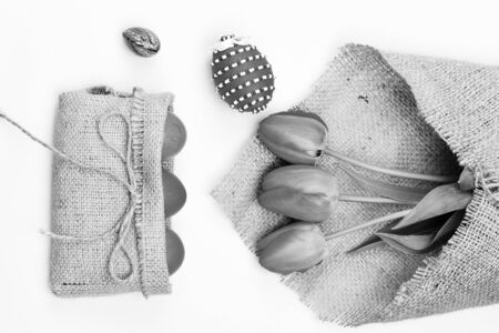 Bunch of flowers near pink Easter eggs in rustic sackcloth bag with bow. Easter symbols concept. Tulips in pink or red color wrapped in burlap on white background. Bouquet of spring tulips for holidayの写真素材