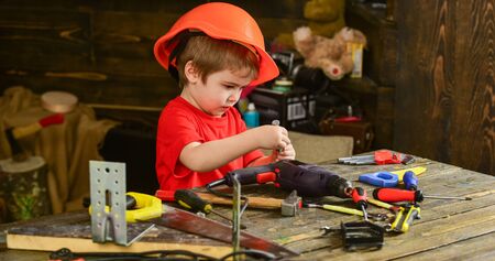 Side view little kid repairing details. Cute boy in orange helmet playing with daddys tools