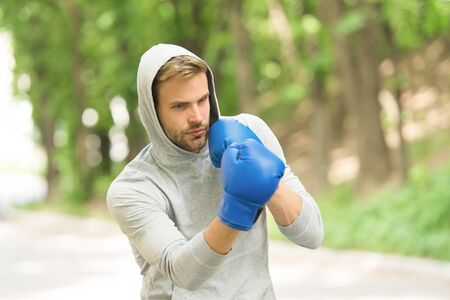 Sharpen his skill. Sportsman concentrated training boxing gloves. Athlete concentrated face sport gloves practice fighting skills nature background. Boxer handsome strict boxing. Sport camp conceptの写真素材