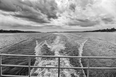 Speed and energy concept. Trace on water in blue sea in manaus, brazil. Sea coast on horizon on cloudy sky. Wanderlust discovery and adventure. Travelling by water.の写真素材