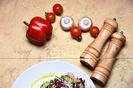 Tomatoes, mushrooms, bell pepper and saltcellar with pepperbox. Appetizer served in restaurant near decor. Ingredients lying by lettuce and chicken salad on beige background. Starter meal conceptの写真素材