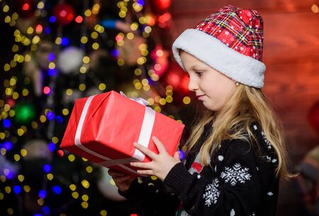 Winter shopping. Holiday party that actually sounds fun. Merry christmas. Kid adorable wear santa hat celebrate christmas. Buy christmas gift. Girl cute child hold wrapped gift near christmas treeの写真素材