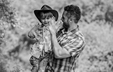 Strong like father. Power being father. Child having fun cowboy dad. Rustic family. Growing cute cowboy. Small helper in garden. Little boy and father in nature background. Spirit of adventuresの写真素材