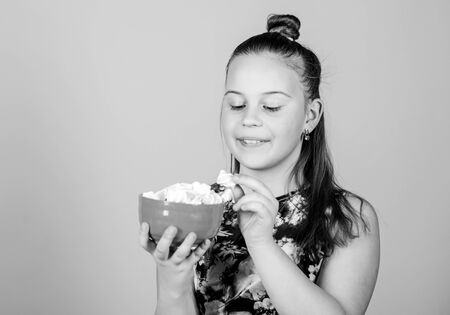 Calorie and diet. Hungry kid. Marshmallow challenge. Girl smiling face hold bowl with sweet marshmallows in hand beige background. Sweet tooth concept. Kid girl with long hair likes sweets and treatsの写真素材