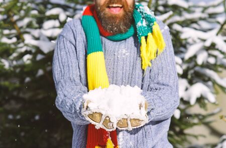 Young man in the snow forest landscape on holiday holding natural soft white snow in his hands to make a snowball, smiling during a cold winter day in the forest, outdoors.の写真素材
