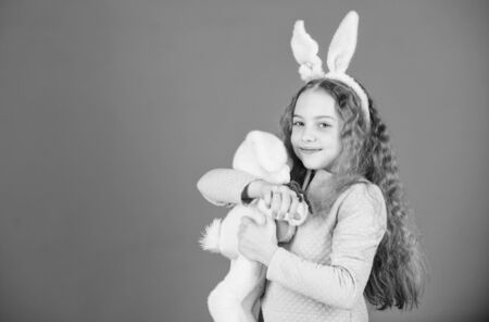 Cute and adorable. Bunny girl with cute toy on blue background. Child smiling play bunny toy. Happy childhood. Get in easter spirit. Bunny ears accessory. Lovely playful bunny child with long hairの写真素材
