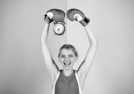 Boxer fighting with alarm clock. Time for boxing training. Punctuality and personal efficiency. Control time. Time management skills. Battle for self discipline. Woman holding clock boxing glovesの写真素材