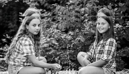 Cognitive development. Intellectual game. Make decision. Smart children. Little girls play chess. Sisters playing chess. Children play chess outdoors nature background. Sport and hobby conceptの写真素材