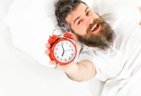 Man with happy face lies on pillow, holds alarm clock.の写真素材