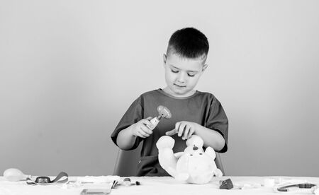 Boy cute child future doctor career. Health care. Kid little doctor busy sit table with medical tools. Medicine concept. Medical procedures for teddy bear. Medical examination. Medical educationの写真素材