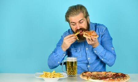 Still hungry. Beer and food. Dinner at pub. Hungry man going to eat pizza french fries and drink beer. Pizzeria restaurant. Cheerful man bearded hipster eat pizza. Pizza party concept. Good appetiteの写真素材
