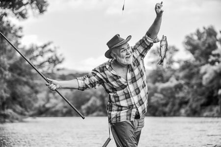 Hobby sport activity. Fish farming pisciculture raising fish commercially. Pensioner leisure. Fish on hook. Man senior fisherman. Fisherman fishing equipment. Fisherman alone stand in river waterの写真素材