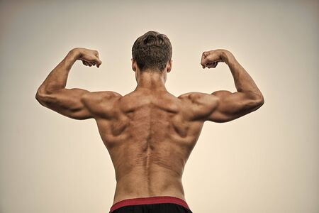 Athlete with bare torso on grey sky. Bodybuilder showing muscles, biceps and triceps. Man or sportsman flexing arms with fists, back view. Fitness and sport. Healthy lifestyle conceptの写真素材