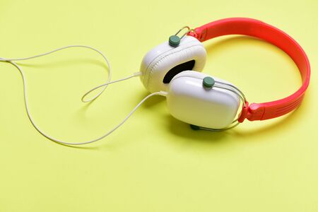 Headset for music made of plastic. Music accessories and technology concept. Modern and stylish earphoneson light yellow background. Headphones in white and red color with long wireの写真素材