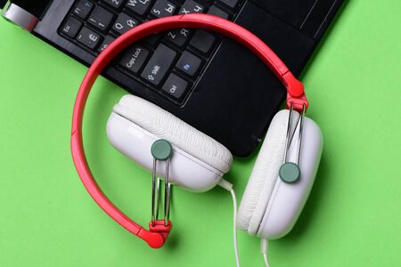Electronics isolated on light green background, top view. Music and digital equipment concept. Headphones and black laptop. Earphones made of plastic with computer. Sound recording idea.の写真素材