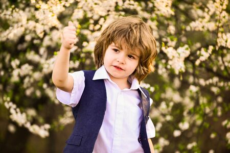 small boy at blossoming spring tree. happy kid has lush healthy hair. summer and spring fashion....