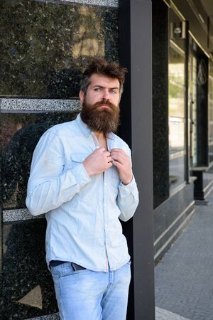 Masculinity concept. Guy looks thoughtful. Hipster with tousled hair unbuttoning shirt on hot day. Man with beard and mustache on thoughtful, pensive face, black marble background.の写真素材
