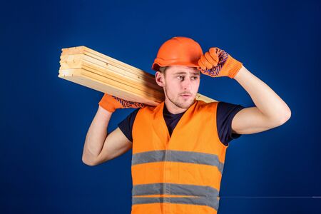 Carpenter, woodworker, labourer, builder carries wooden beam on shoulder. Man in protective gloves...