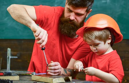 Father, parent with beard teaching little son to use tool screwdriver. Boy, child busy in protective...