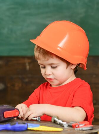 Toddler on busy face plays with bolts at home in workshop. Kid boy play as handyman. Child in hard hat, helmet playing with hex bolts as builder or repairer, handcrafting. Handcrafting concept.の写真素材