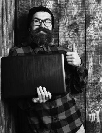 Bearded brutal caucasian hipster holding laptop on brown vintage wooden studio backgroundの写真素材