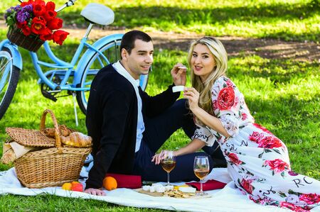 Give uncommon, unique gifts spontaneously. Enjoying their perfect date. Couple in love picnic date. Spring weekend. Happy loving couple relaxing in park with food. Romantic picnic with wineの写真素材