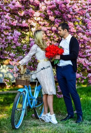 Gift with love. dog in retro bicycle date. romantic couple under sakura tree. couple in love with vintage bike. spring flower bloom. man and woman in park with pink blossom. beauty and fashionの写真素材