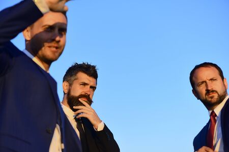 Businessmen with serious faces in suits on blue sky background.の写真素材