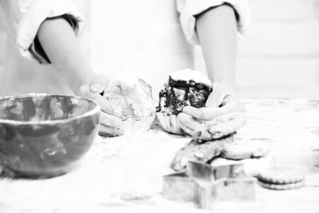 young male hands of cook chef in white uniform standing near table with red bowl lot of flour and holding tasty cakes or muffins with powdered sugar, on brick wall backgroundの写真素材