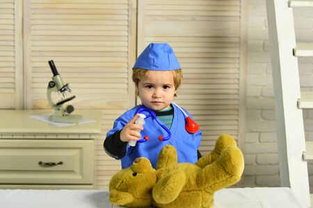 Kid in doctor coat makes injection to teddy bear.