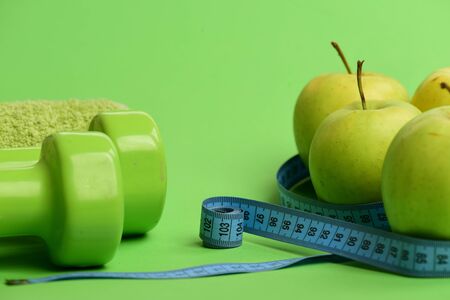 Sports and healthy regime equipment, copy space. Dumbbells in green color, rolled measure tape, towel and fruit on green background. Barbells near juicy green apples. Athletics and weight loss conceptの写真素材