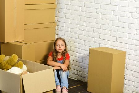 Kid sits on floor in corner. Girl with serious faceの写真素材