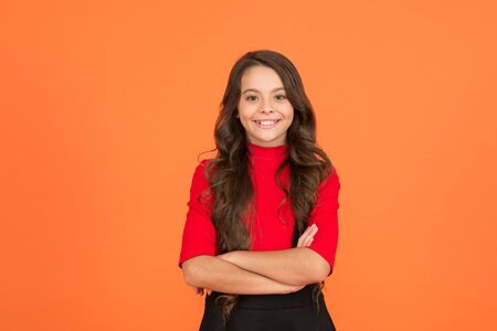 Optimistic concept. Good vibes. Happy childhood. Healthy smile. Feeling lucky. Perfect girl. Positive emotions. Teen girl smiling orange background. Teen child with long curly hair. Back to schoolの写真素材