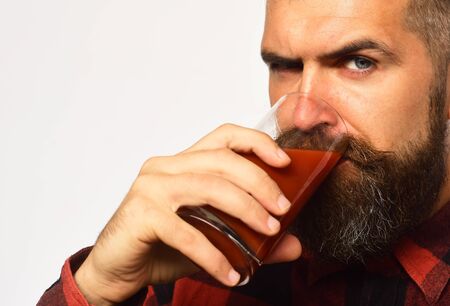 Farmer with serious face drinks glass of fresh red juice. Farming and autumn products concept. Man with beard holds tomato juice isolated on white background. Guy shows his harvestの写真素材