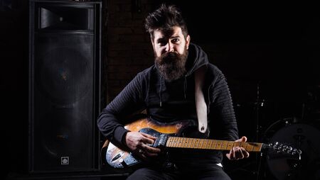 Man in black clothes holds guitar, play music near speakers,