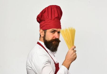 Cook with tricky face in burgundy uniform holds dry pastaの写真素材